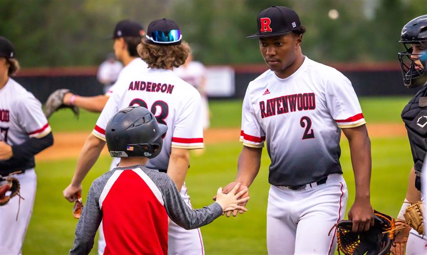 A Ravenwood High baseball player high fives a young boy.